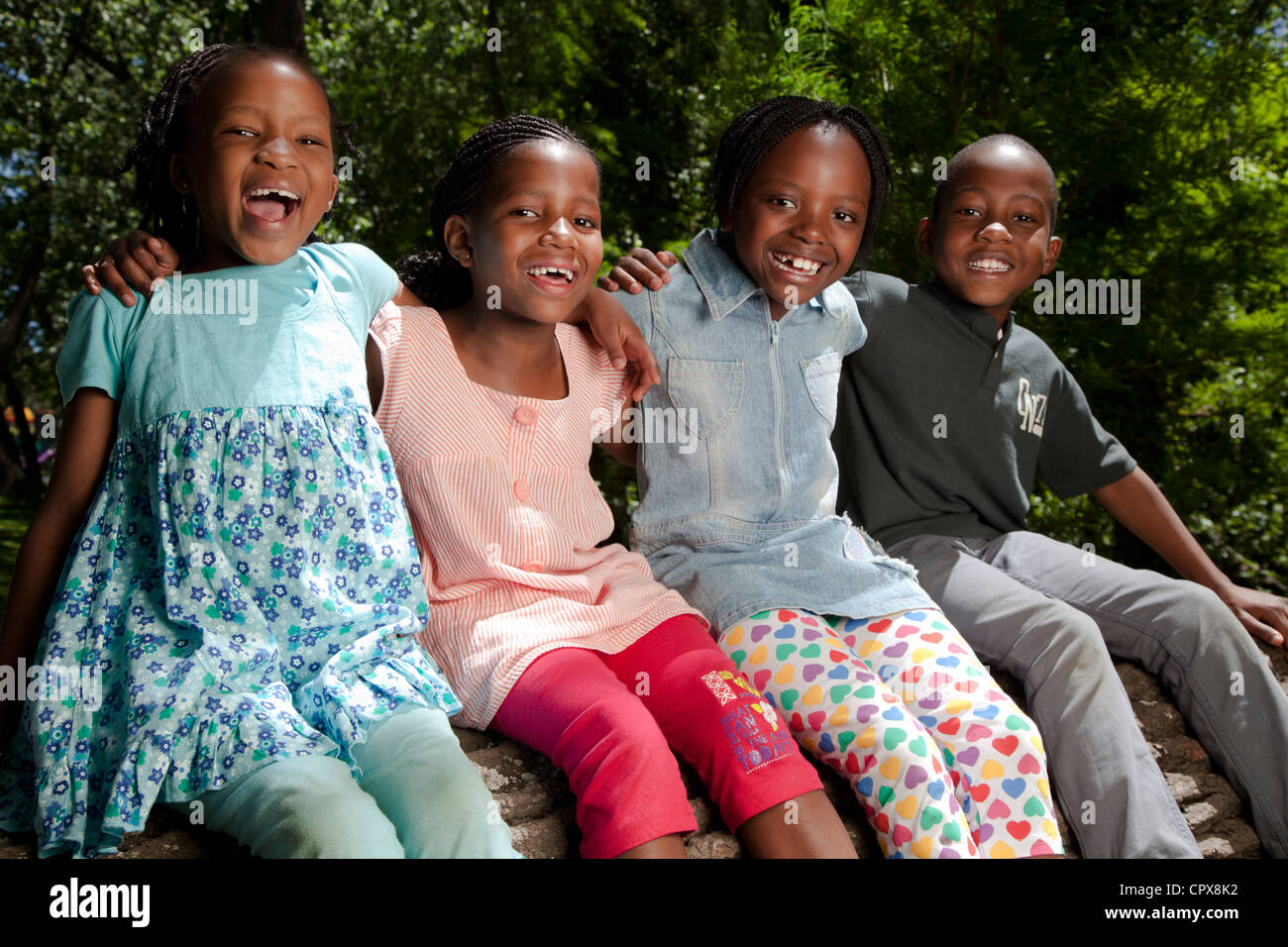 Vier Kinder sitzen auf einem Baumstamm in einem park Stockfoto