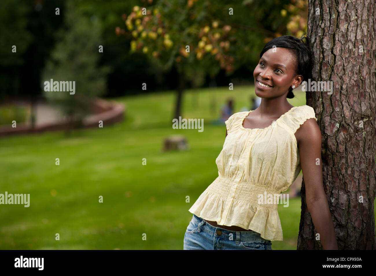 Junge afrikanische Frau gegen einen Baum in einem Park, Lächeln Stockfoto