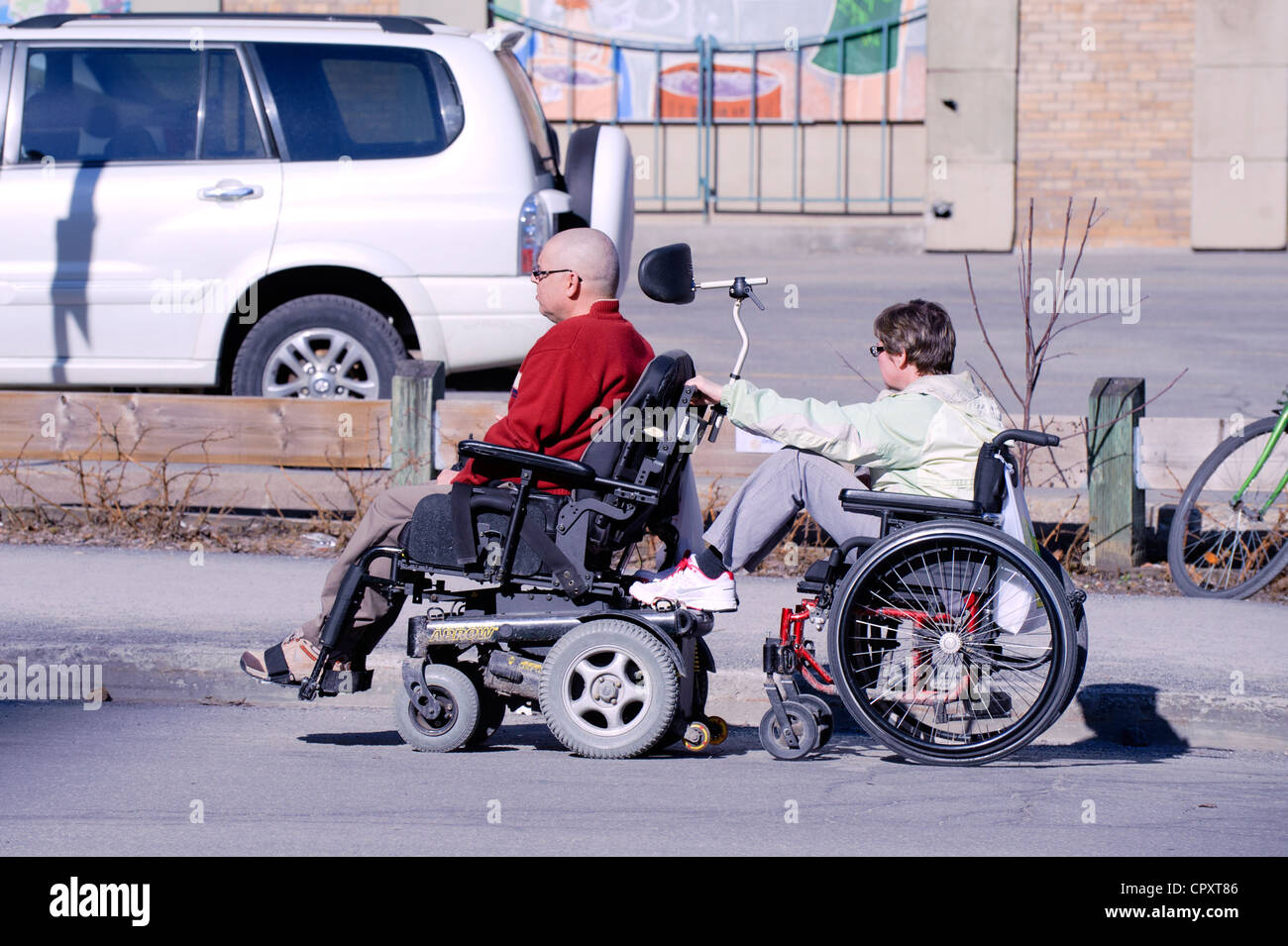 Paar im Rollstuhl in einer Straße der Innenstadt von Montreal. Die Frau Stuhl ist hinter durch des Mannes gezogen, was motorisiert ist. Stockfoto