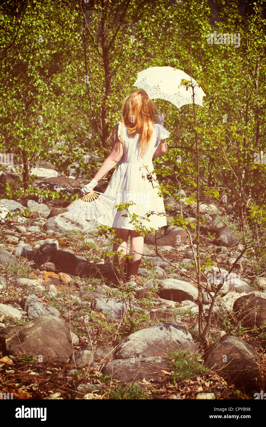 Junge Frau mit einem Ventilator und einem Sonnenschirm durch einen Wald laufen Stockfoto