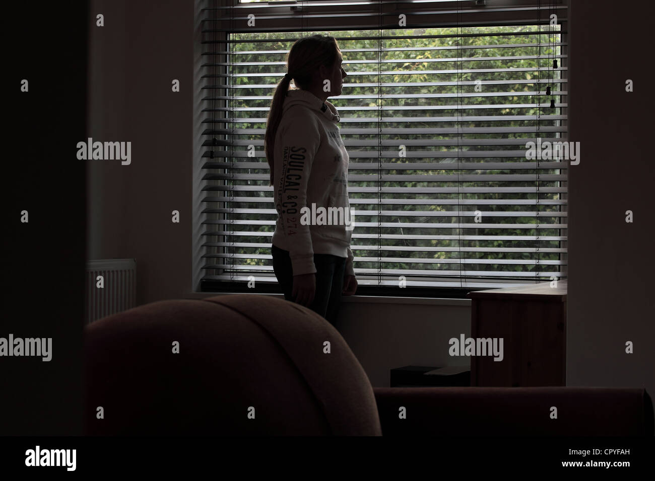 Junge Frauen stehen in einem dunklen Raum mit Blick durch ein Fenster blind. Stockfoto