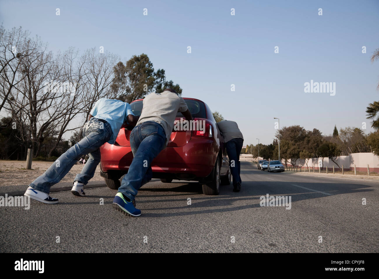 Zwei Männer, ein Auto zu schieben, während ein Drittel es lenkt Stockfoto