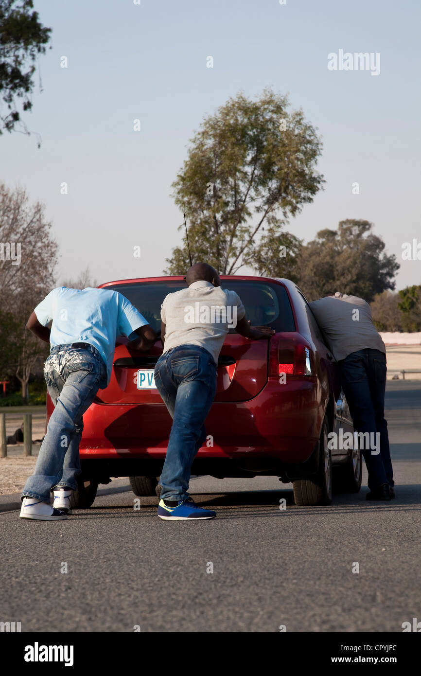 Zwei Männer, ein Auto zu schieben, während ein Drittel es lenkt Stockfoto