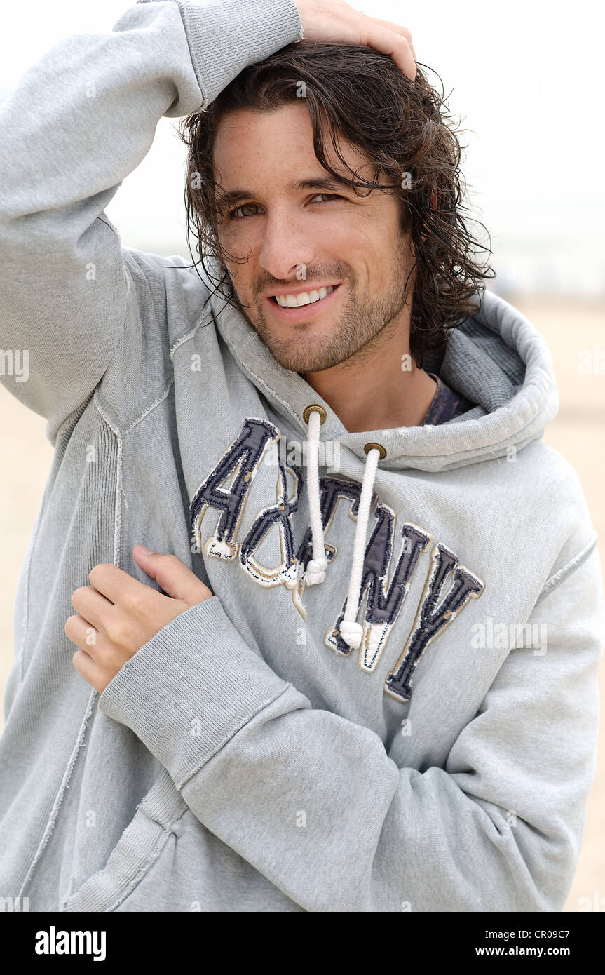 Mann, Anfang 30, trägt einen Kapuzensweater bei schlechtem Wetter am Strand Stockfoto