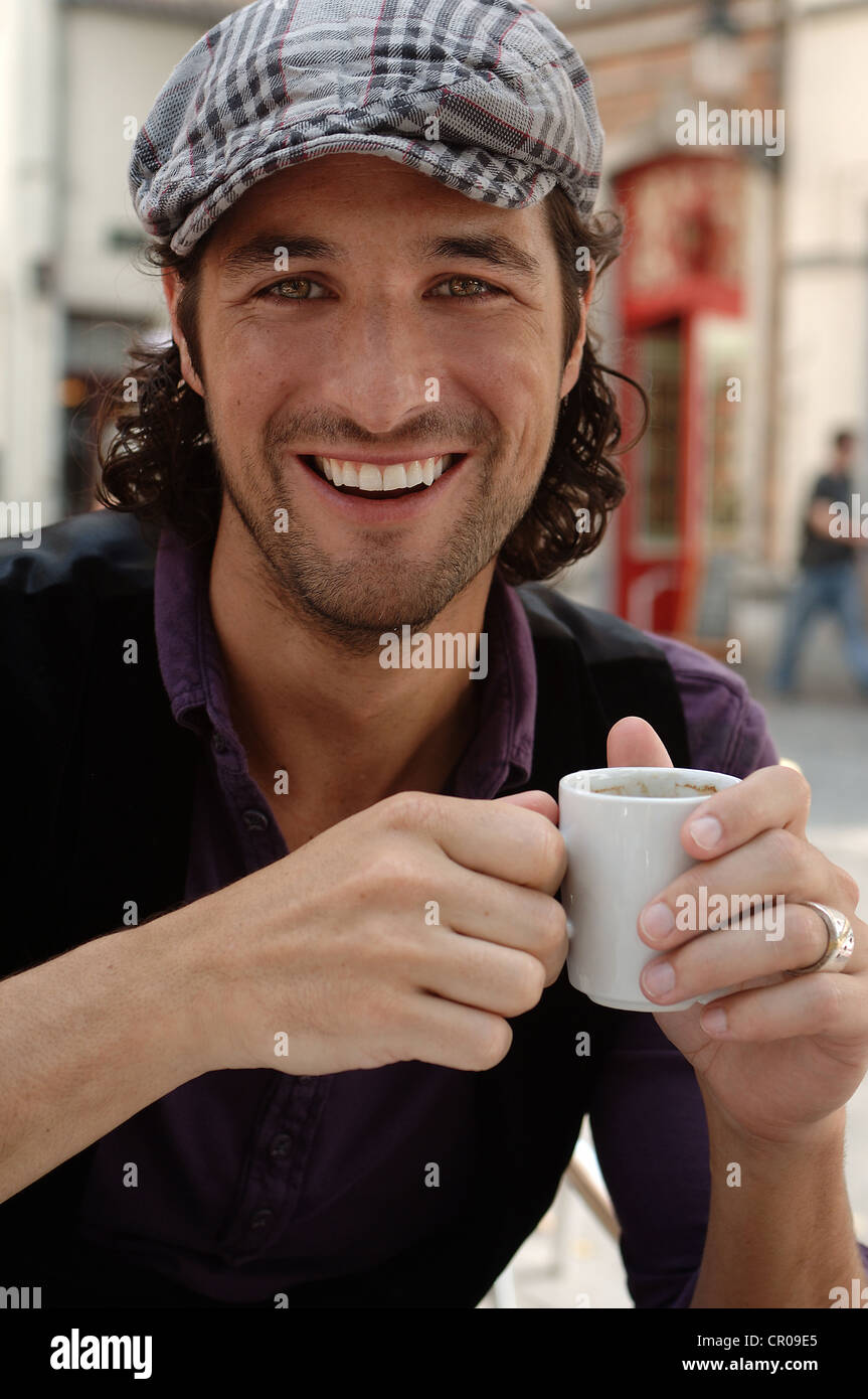 Mann, Anfang der 30er Jahre, tragen legere Kleidung, sitzen in einem Straßencafé hält eine Kaffeetasse lächelnd Stockfoto