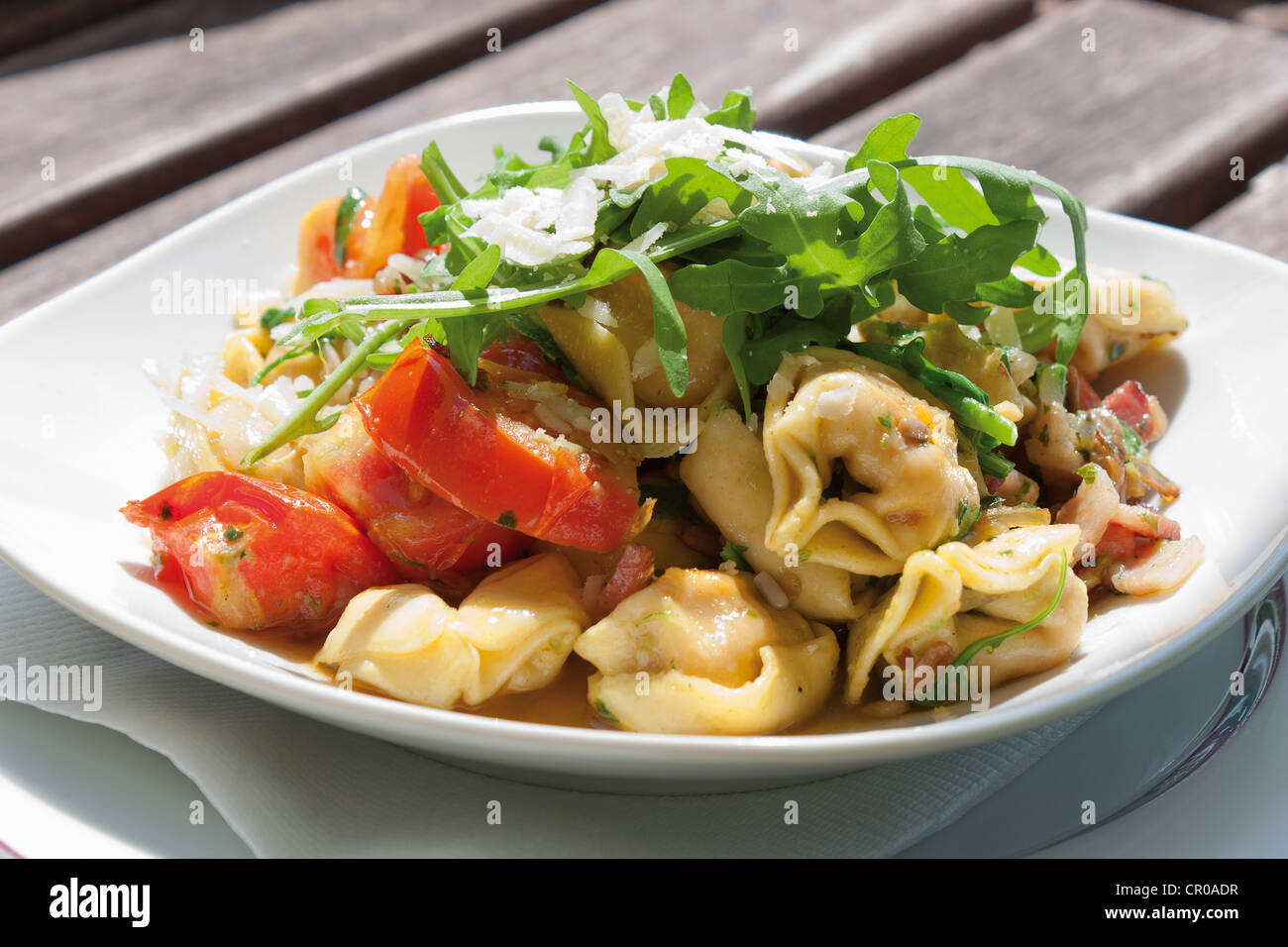 Tortellini mit Rucola-Salat, Speck, frische Tomaten und gerösteten Sonnenblumenkernen Stockfoto