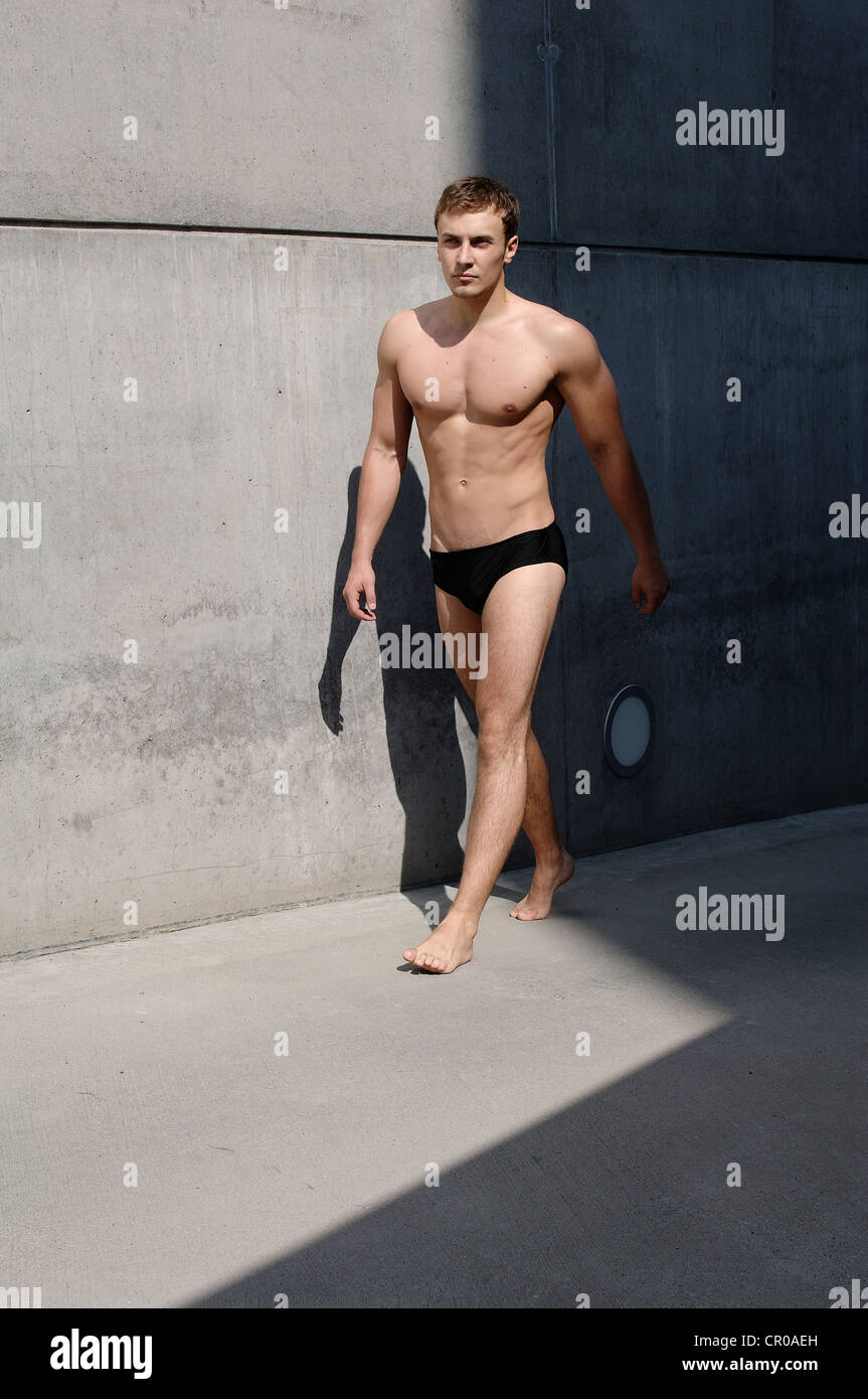 Junger Mann tragen Badehosen zu Fuß vor einer Betonwand Stockfoto