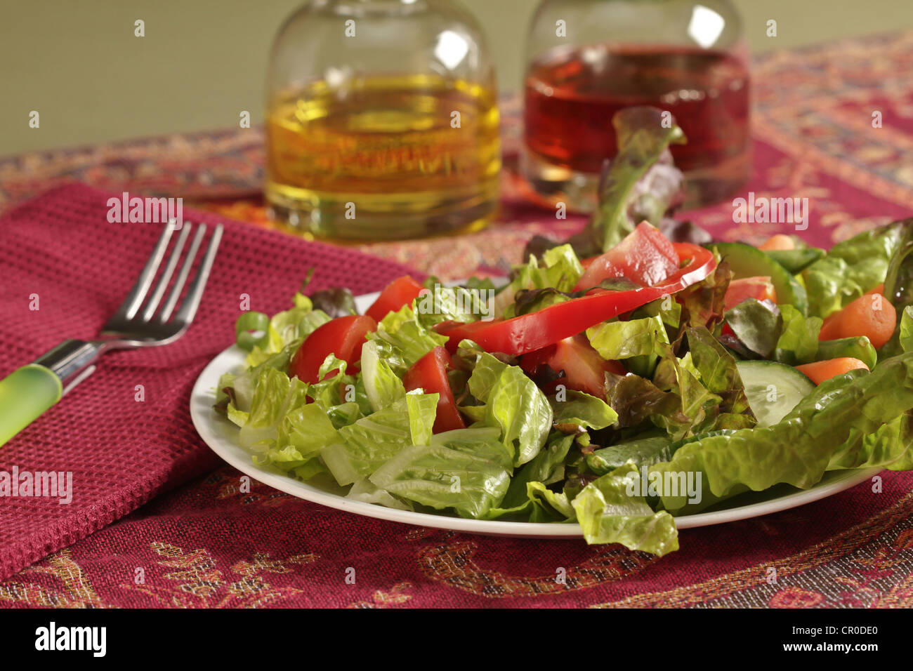 Eine einfache gemischter Salat mit Tomaten, Paprika, Karotten und eine Menage Essig und Öl auf rosa farbigen Tischset mit Gabel. Stockfoto