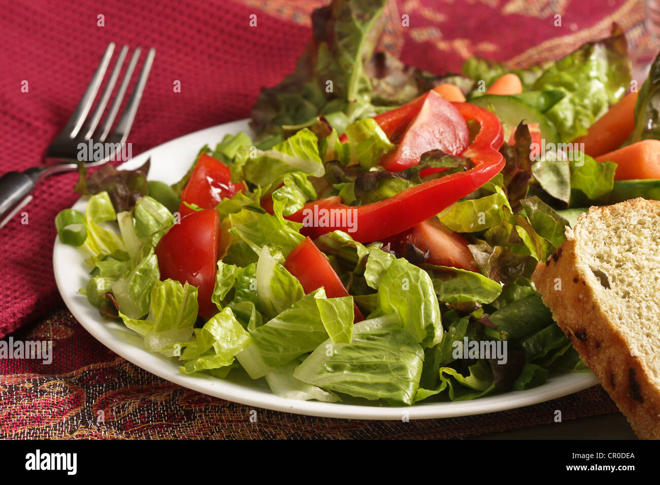 Eine Nahaufnahme von einem gemischten Salat mit Tomaten, Paprika, Karotten und Seite von Brot auf eine Rose farbige Tischdecke mit einer Gabel einstechen. Stockfoto