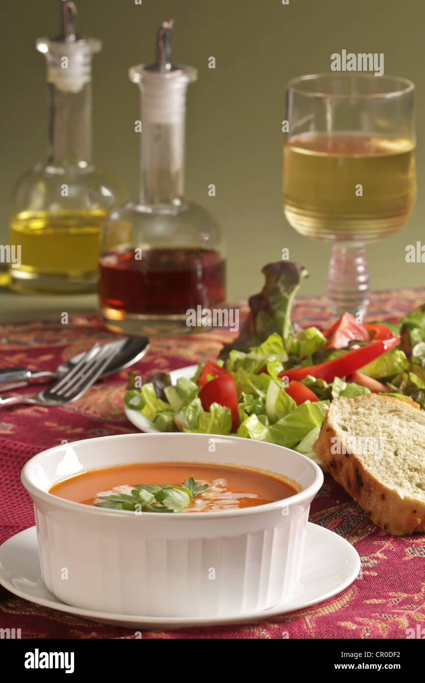 Ein Gedeck für das Mittagessen Tomatensuppe und gemischter Salat mit Brot und einem Glas Wein, Crucis aus Öl und Essig. Stockfoto