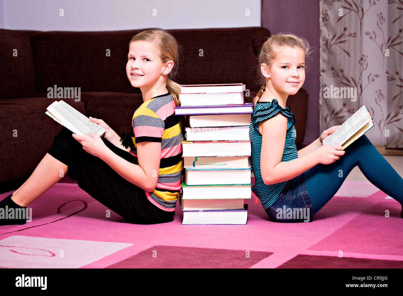 Mädchen, 11 und 8, lehnte sich gegen einen Stapel Bücher Stockfoto