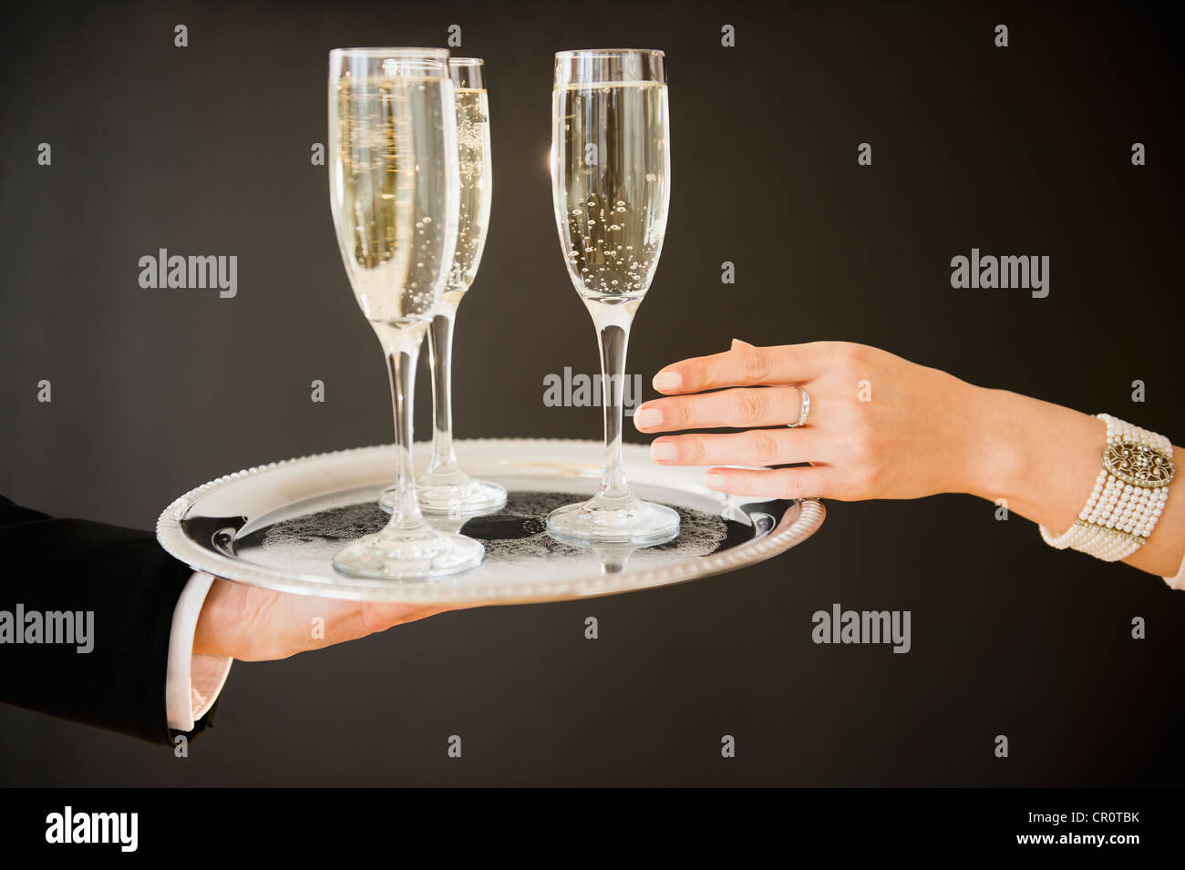 Nahaufnahme eines Mannes und Weibes Hände und Tablett mit Champagner-Flöten, Studio gedreht Stockfoto
