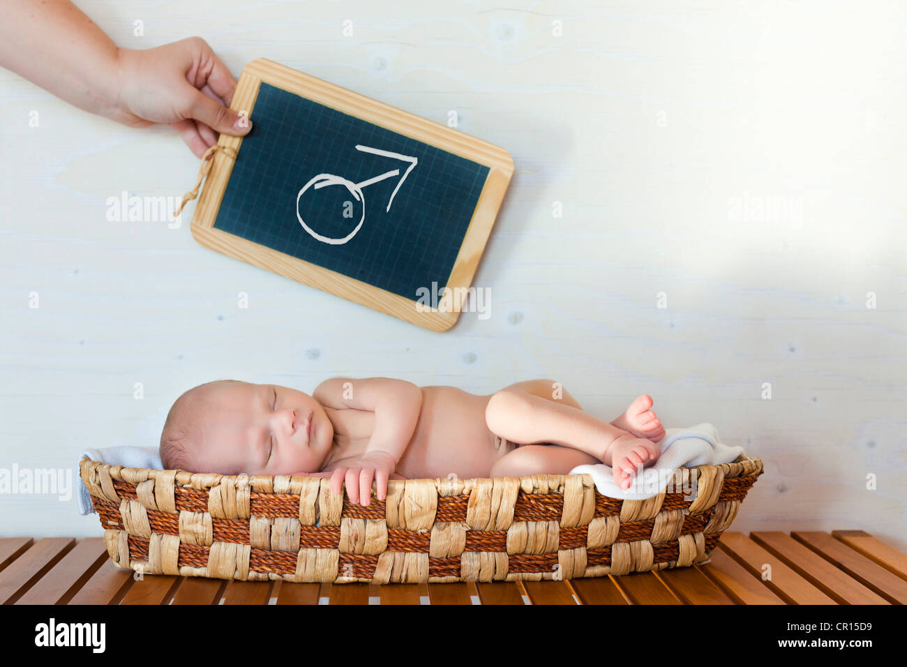 Neugeborenes Baby, 3 Wochen, mit einer Hand hält eine Tafel mit einem Mars-Symbol oben in einem Korb schlafen Stockfoto