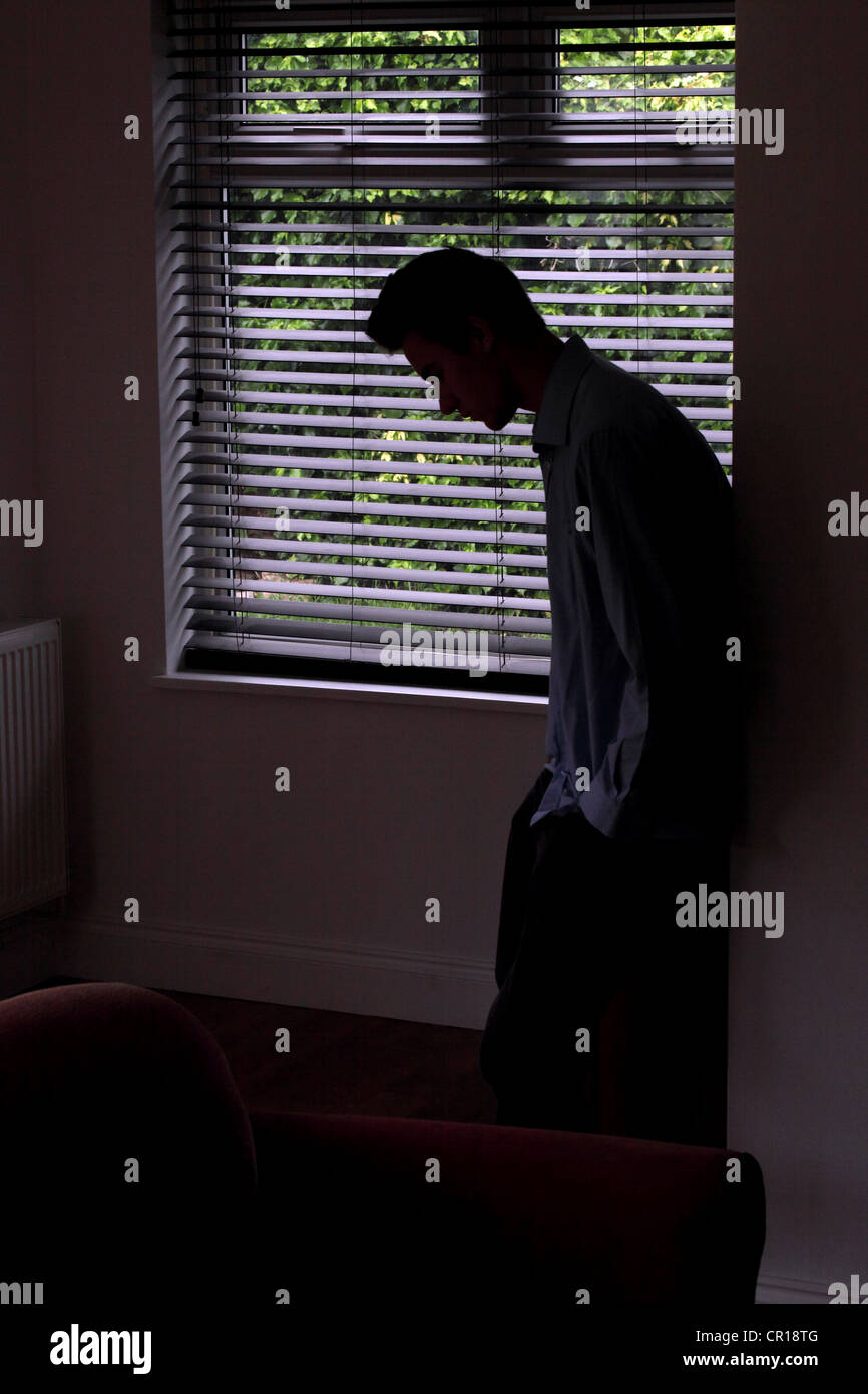 Silhouette des jungen männlichen lehnt gegen eine Wand durch ein Fenster. Stockfoto