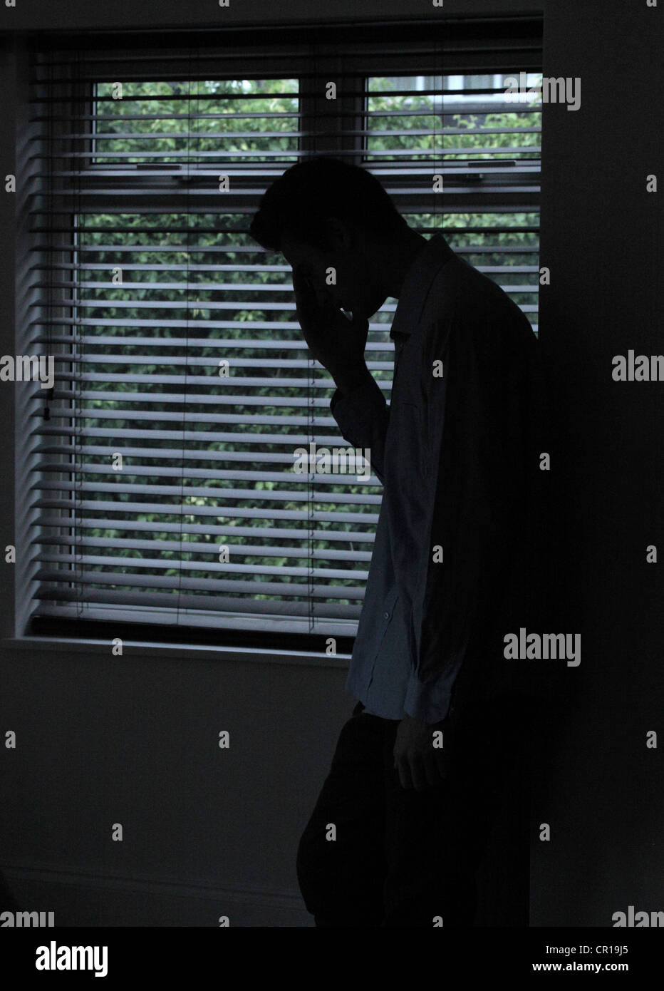 Silhouette eines männlichen stehenden in einem dunklen Raum mit Licht aus einem Fenster mit Jalousien, seine Gestalt, Hand, Gesicht zu zeigen. Stockfoto