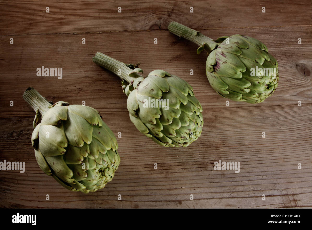 Drei Artischocken (Cynara Cardunculus) auf einem Holzbrett Stockfoto