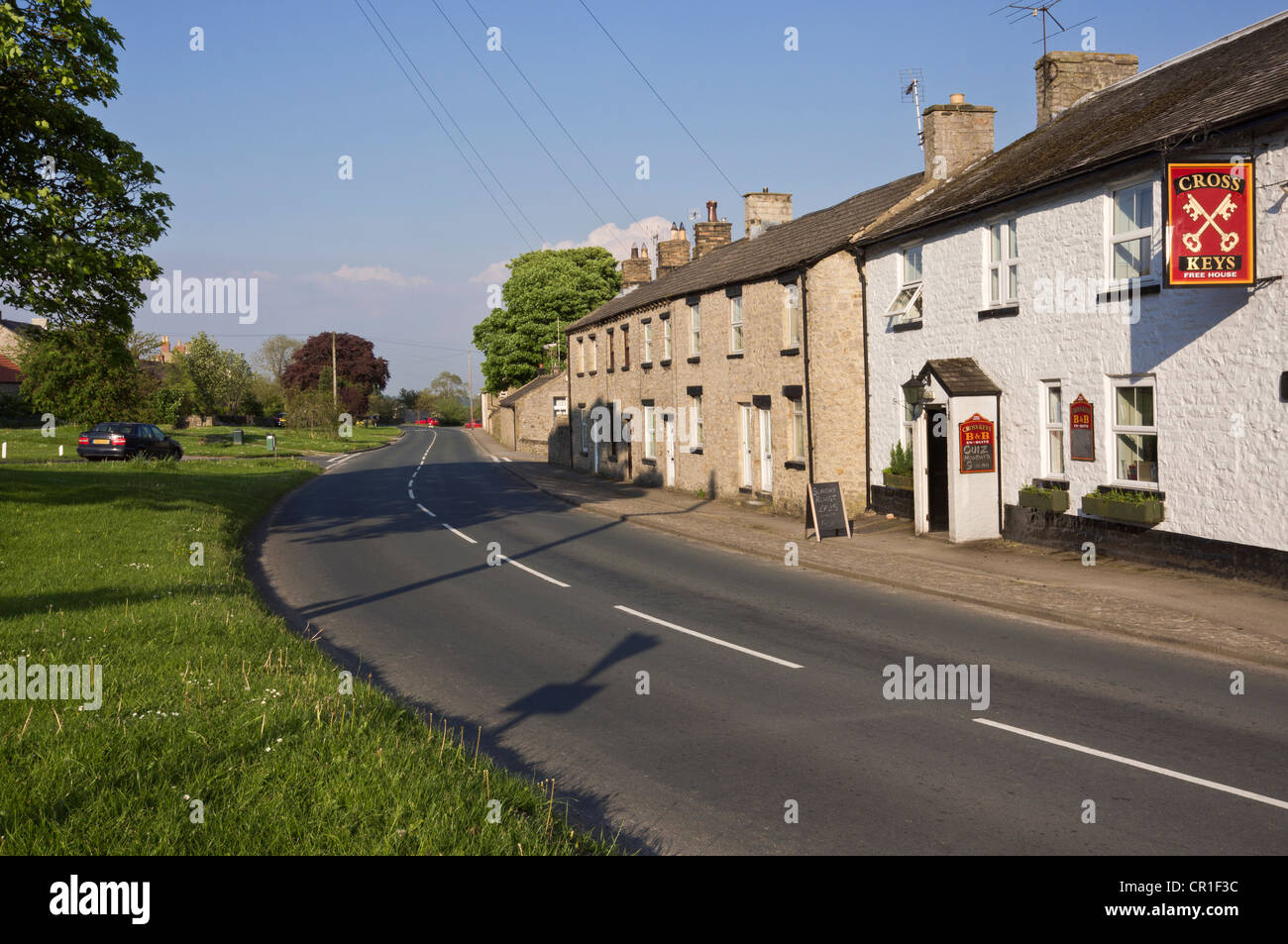 Bellerby, in der Nähe von Leyburn, North Yorkshire. Straße durch den Dorfanger mit Pub (The Cross Keys) und Häuser. Stockfoto