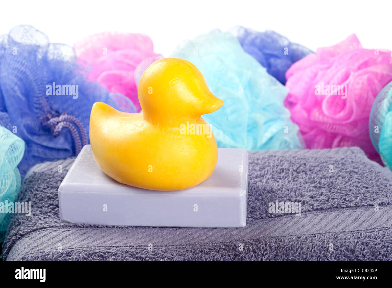 Eine Ente geformt Stück Seife ruht auf einem lila Badetuch mit bunten Dusche Hocker auf weiß. Stockfoto