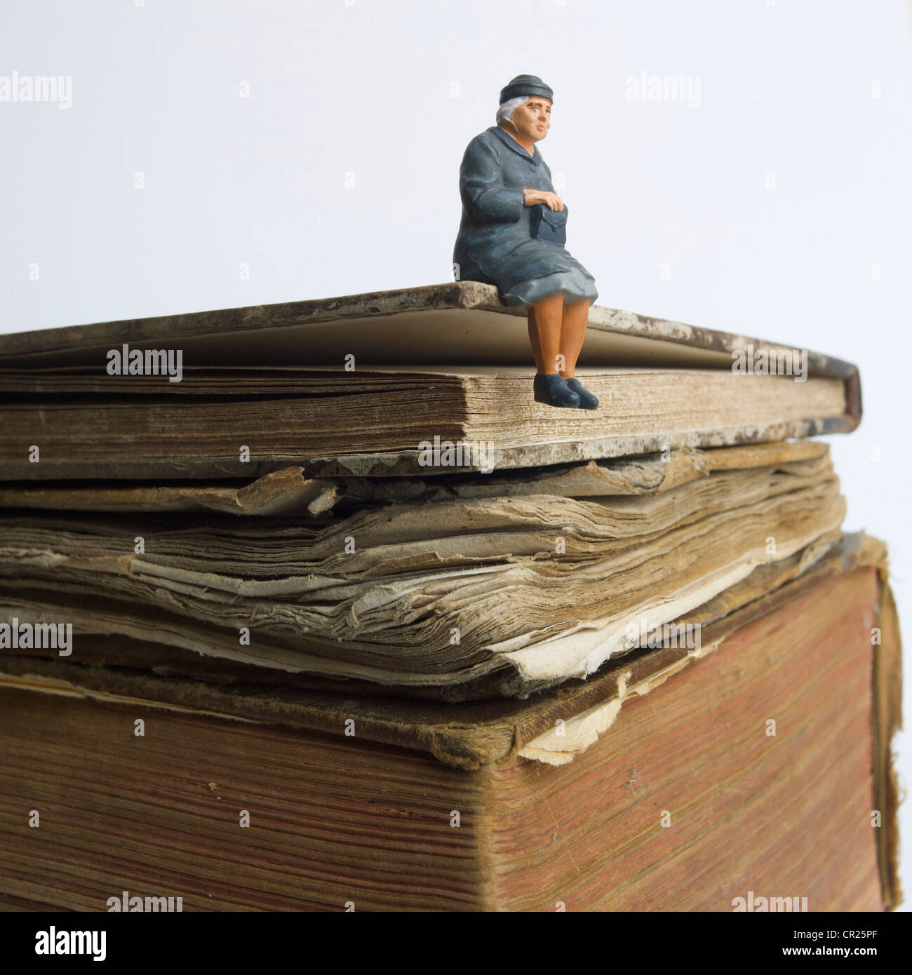 Ältere Dame, Miniatur Figur, sitzt auf einem alten Buch - wissen / Weisheit / Lebensgeschichte Konzept. Stockfoto