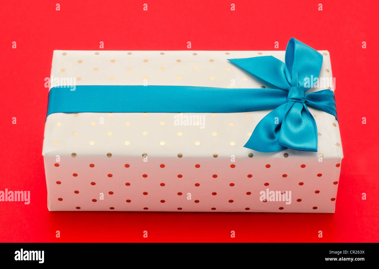 Verpackte Geschenkbox mit einem blauen Band und Schleife - Schuss von oben in das Studio mit einem roten Hintergrund Stockfoto