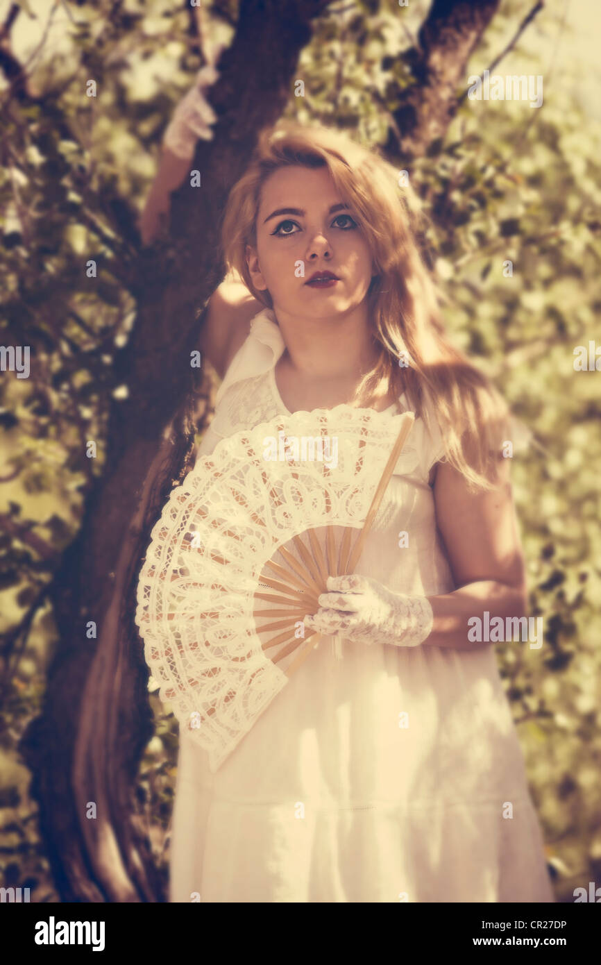 junge Frau im weißen Kleid mit einem Ventilator im Wald Stockfoto