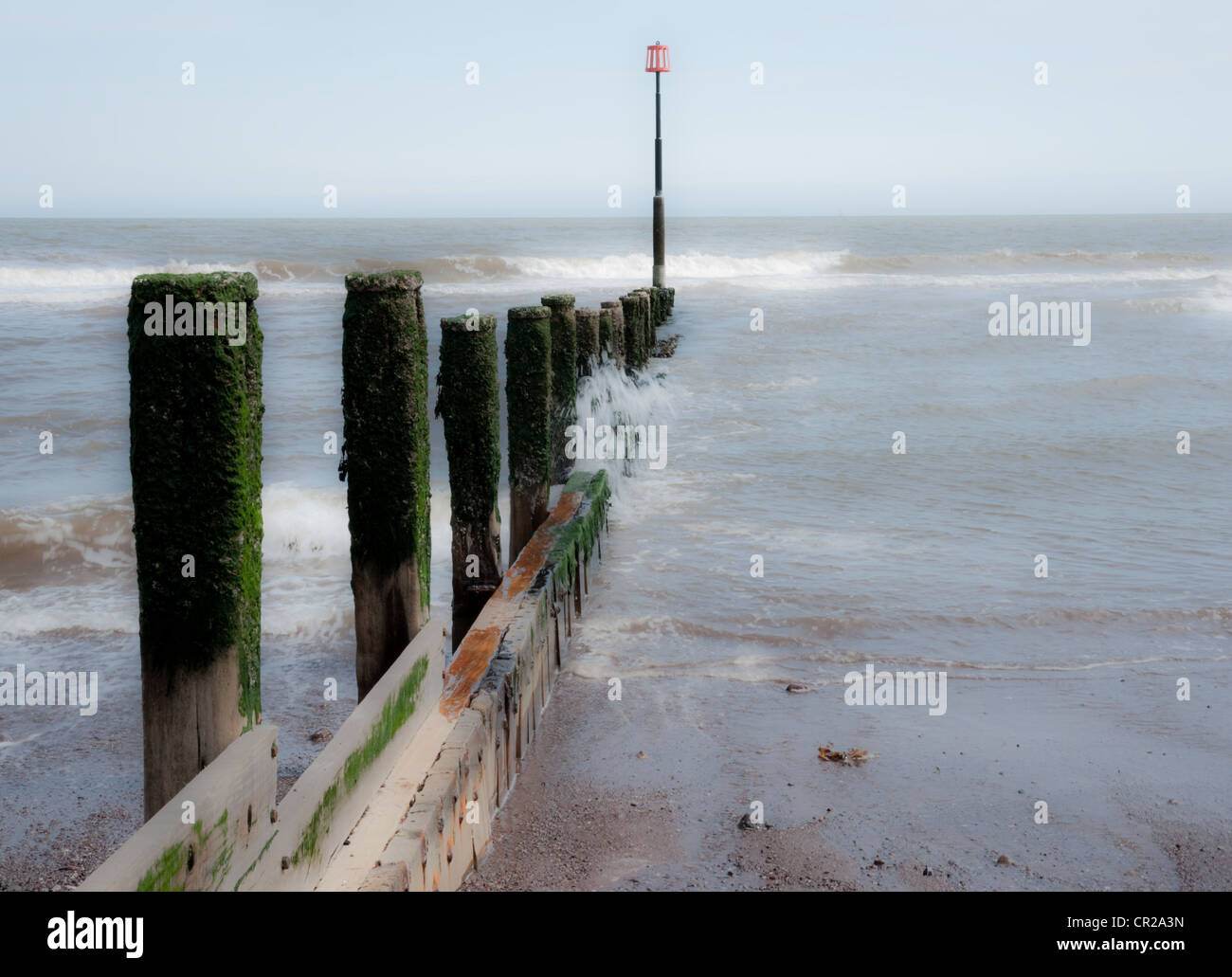 Eine altmodische hölzerne Wellenbrecher erstreckt sich in das Meer von einem Sandstrand entfernt. Stockfoto