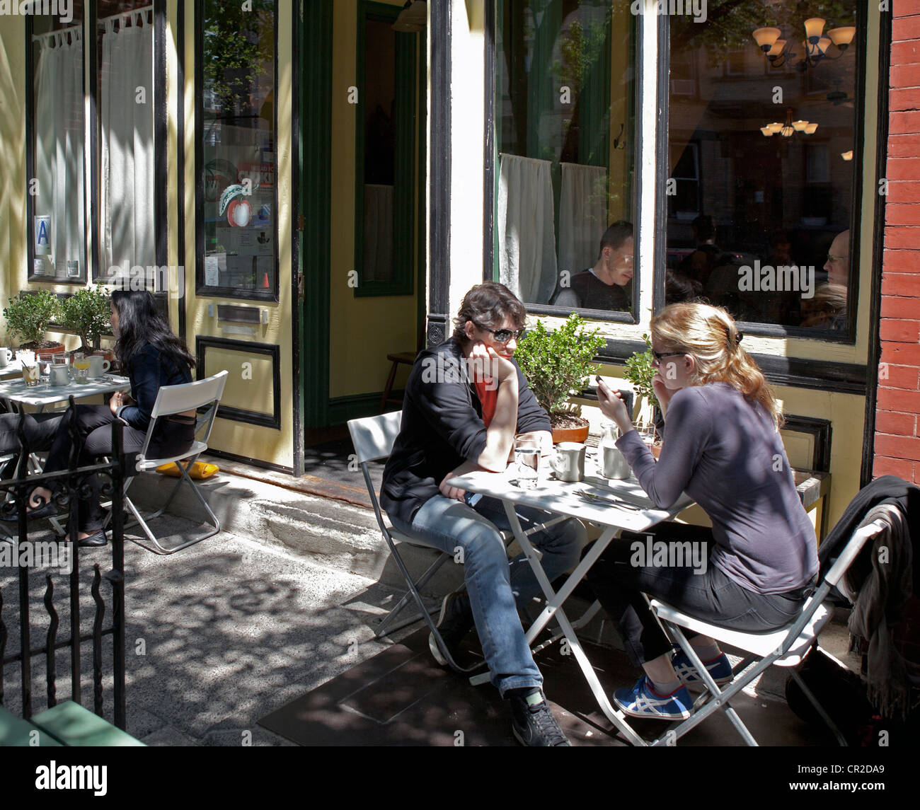 Ein Mann schaut genervt, während seine Begleiter auf dem Handy in einem Restaurant im Stadtteil Park Slope, Brooklyn, New York ist. Stockfoto