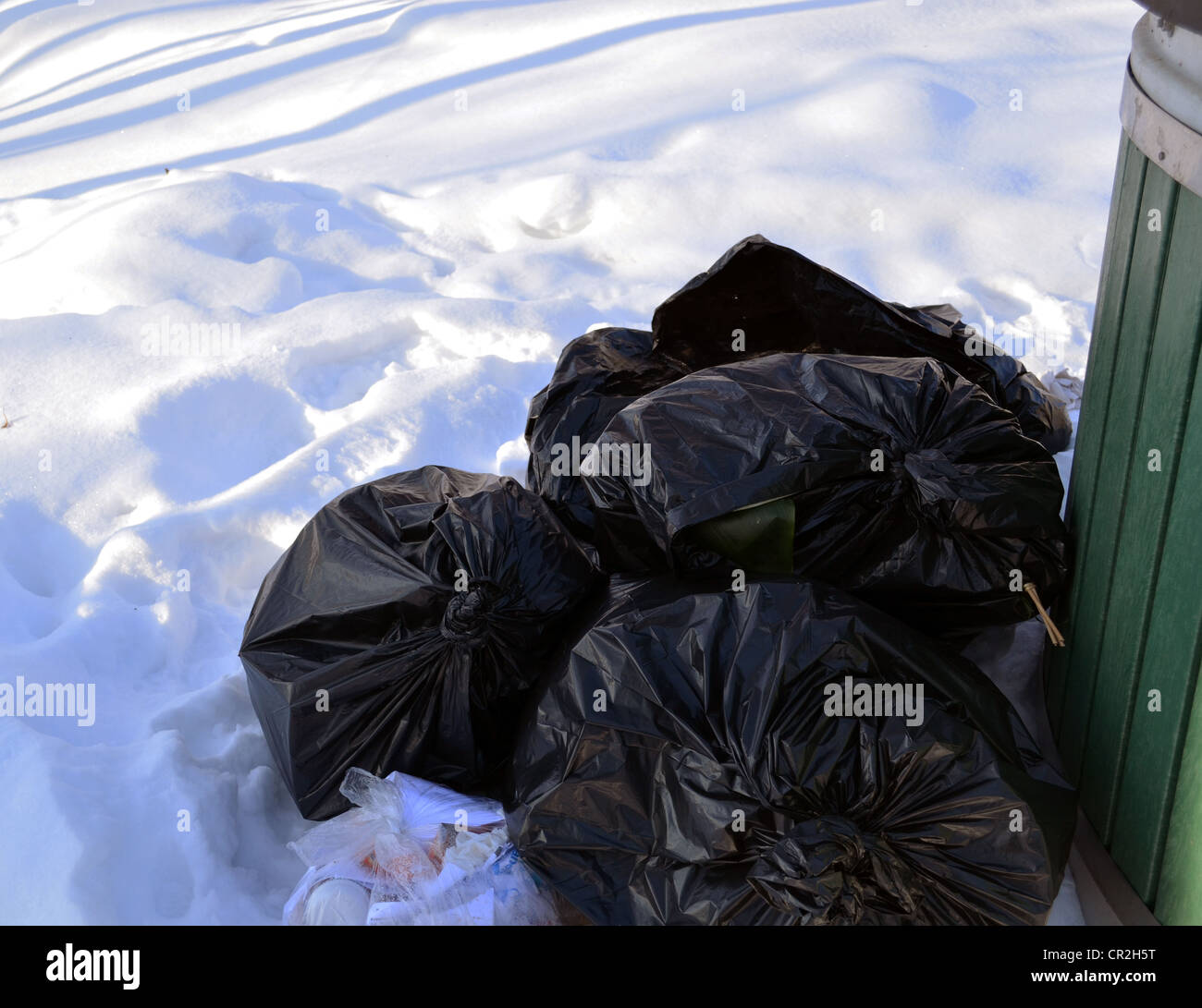 Schwarze Müllsäcke auf Schnee neben Müllcontainer im Winter. Stockfoto