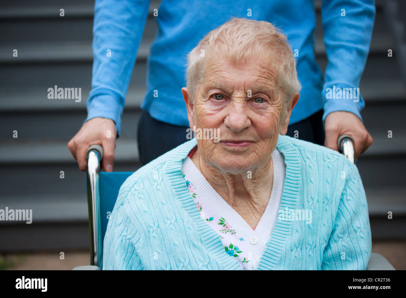 Senior-Frau im Rollstuhl mit Assistent hinter ihr. Stockfoto