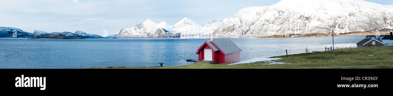 Kleine rote Hütte am Fuß eines Sees mit schneebedeckten Bergen im Hintergrund Stockfoto