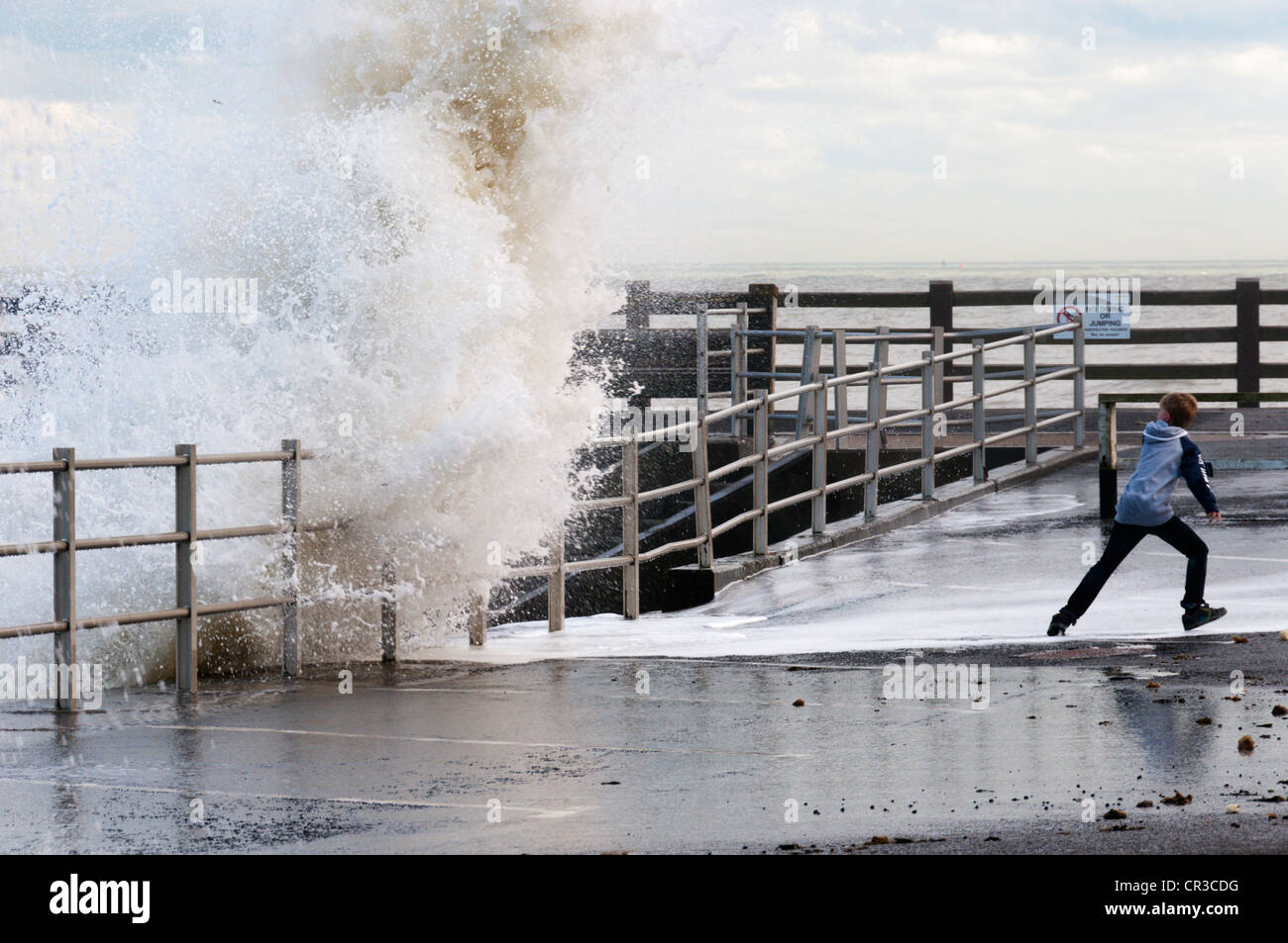 Ein kleiner Junge ausweichen die Wellen brechen über die Hafenmauer in Broadstairs in Kent. Stockfoto