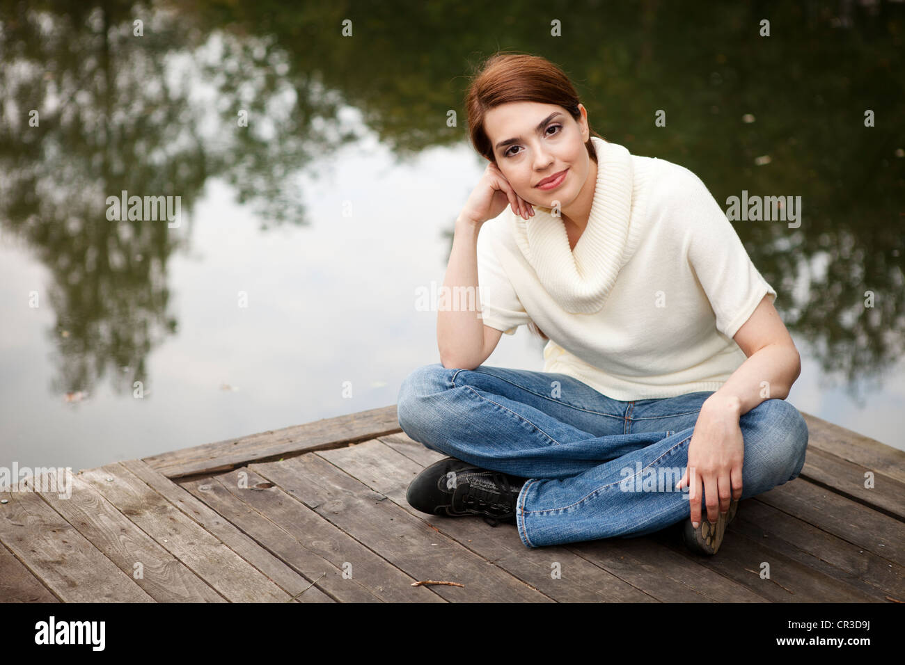 Freundlich lächelnde Mädchen sitzen auf einem Steg am See Stockfoto