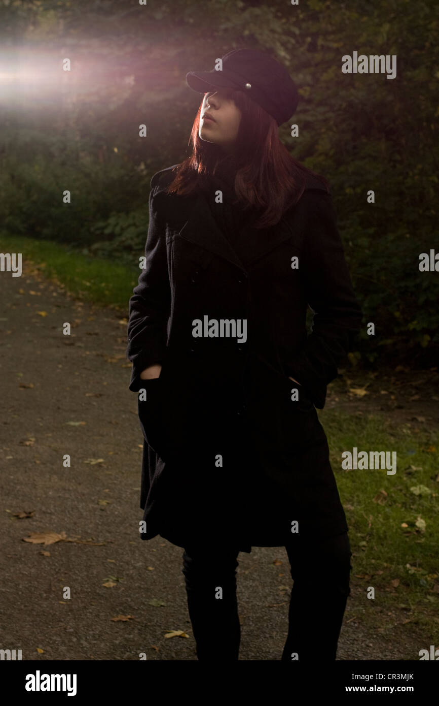 Junge Frau mit Hut stehen in einem dunklen Park, flash Stockfoto