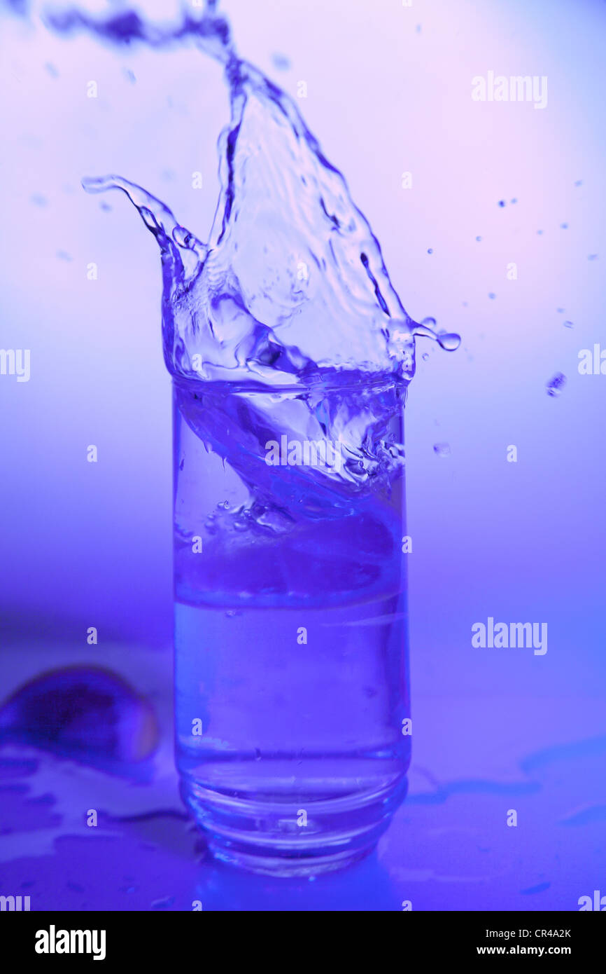 Eine Zitronenscheibe Spritzwasser in ein Glas Wasser unter bunten Lichtern Stockfoto