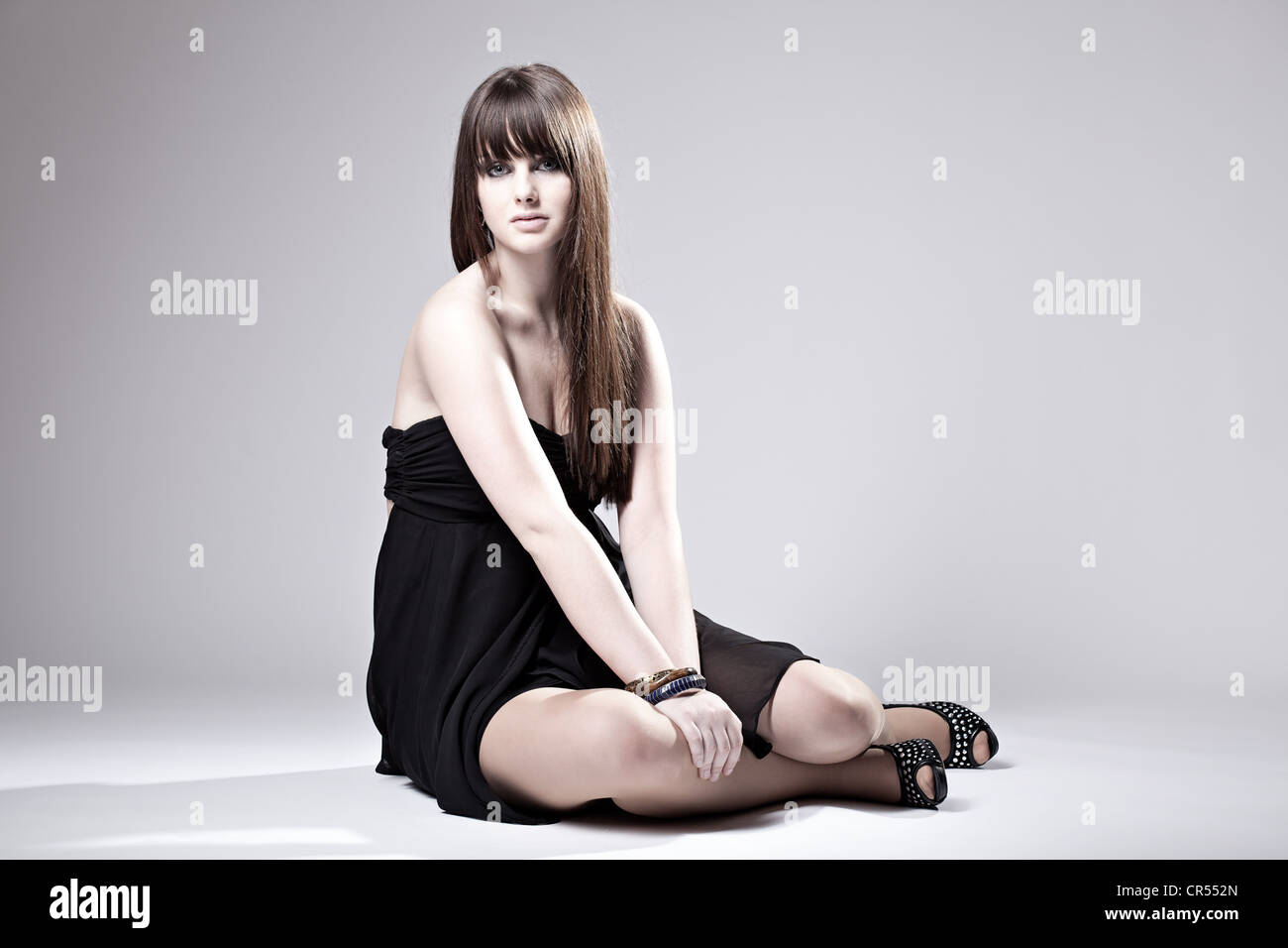 Junge Frau posiert im schwarzen Kleid, sitzen Stockfoto