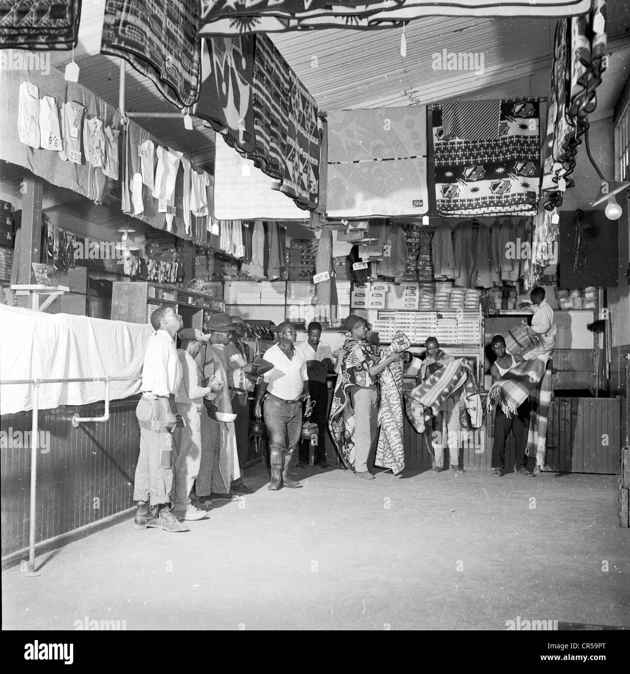 1950er Jahre, historische, lokale schwarze Landarbeiter im Laden, die Materialien und Stoffe in einem ländlichen Laden in Südafrika suchen. Stockfoto