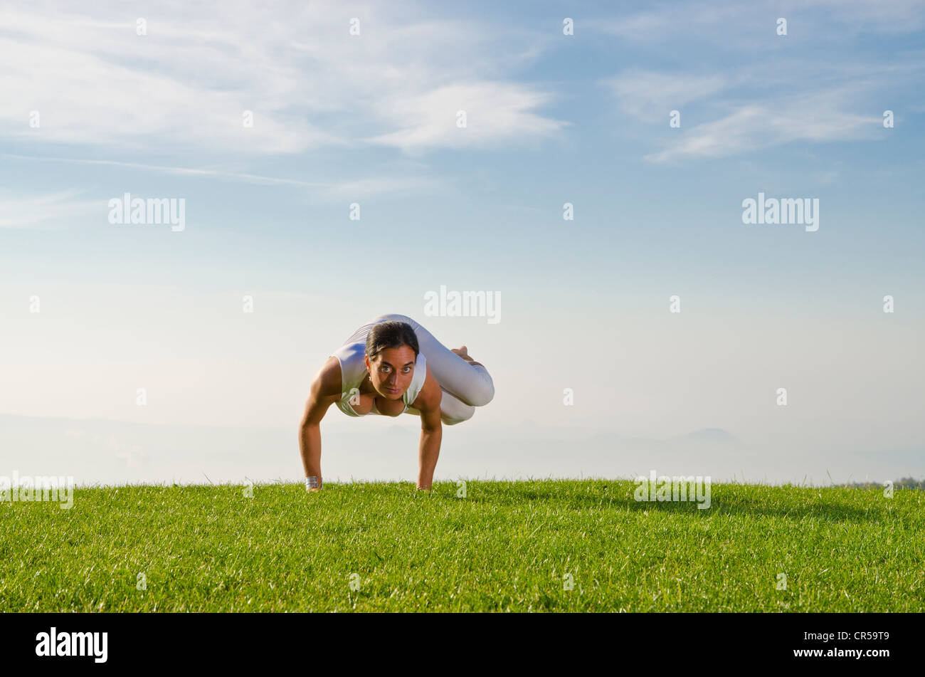 Junge Frau Hatha Yoga im Freien praktizieren, zeigt die Pose Parshva Kakasana, Parshva Bakasana, seitliche Krähe pose Stockfoto