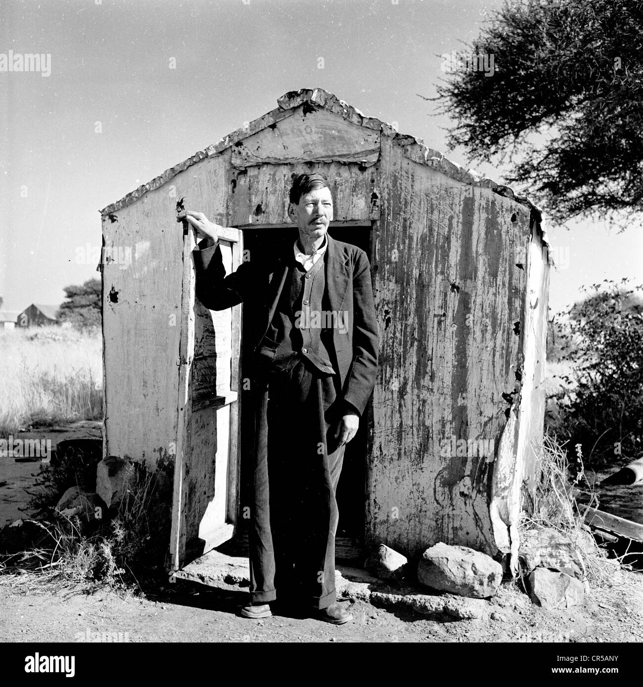 Südafrika, in den 1950er Jahren, steht ein Afrikaner Minenleiter draußen am Eingang seiner Arbeitswohnung, einer kleinen Holzhütte oder Hütte in diesem historischen Foto von J Allan Cash. Im 17. Und 18. Jahrhundert stammten die Afrikaner als Ethikgruppe in Südafrika von europäischen Kolonisten, hauptsächlich holländischen Siedlern, aber auch französischen und deutschen, ab, um die Politik und den Agrarsektor im Land zu dominieren, was bis 1994 dauerte. Stockfoto