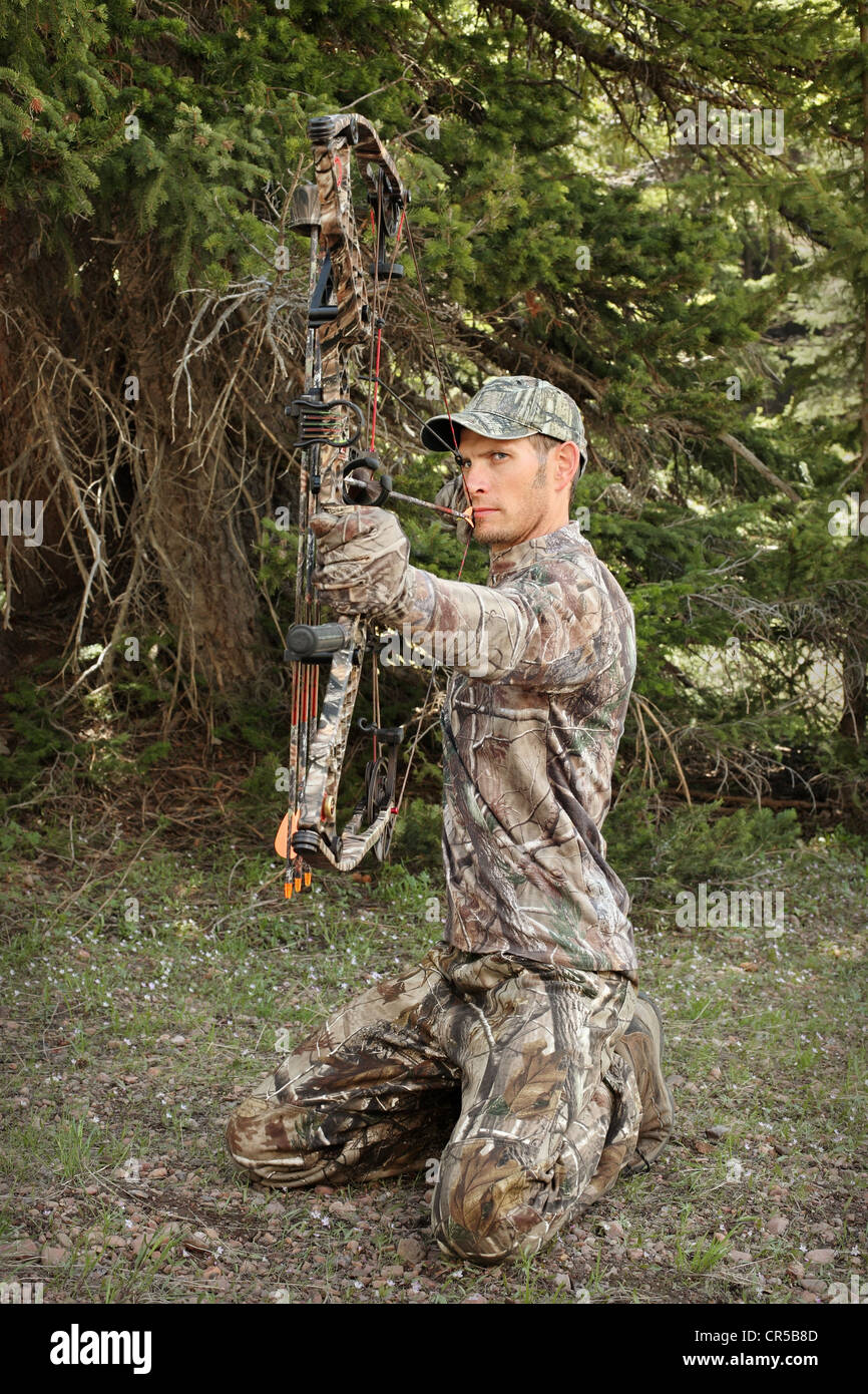 Full-length Bow Hunter tragen Tarnung ziehen Bogen zurück im Wald Stockfoto