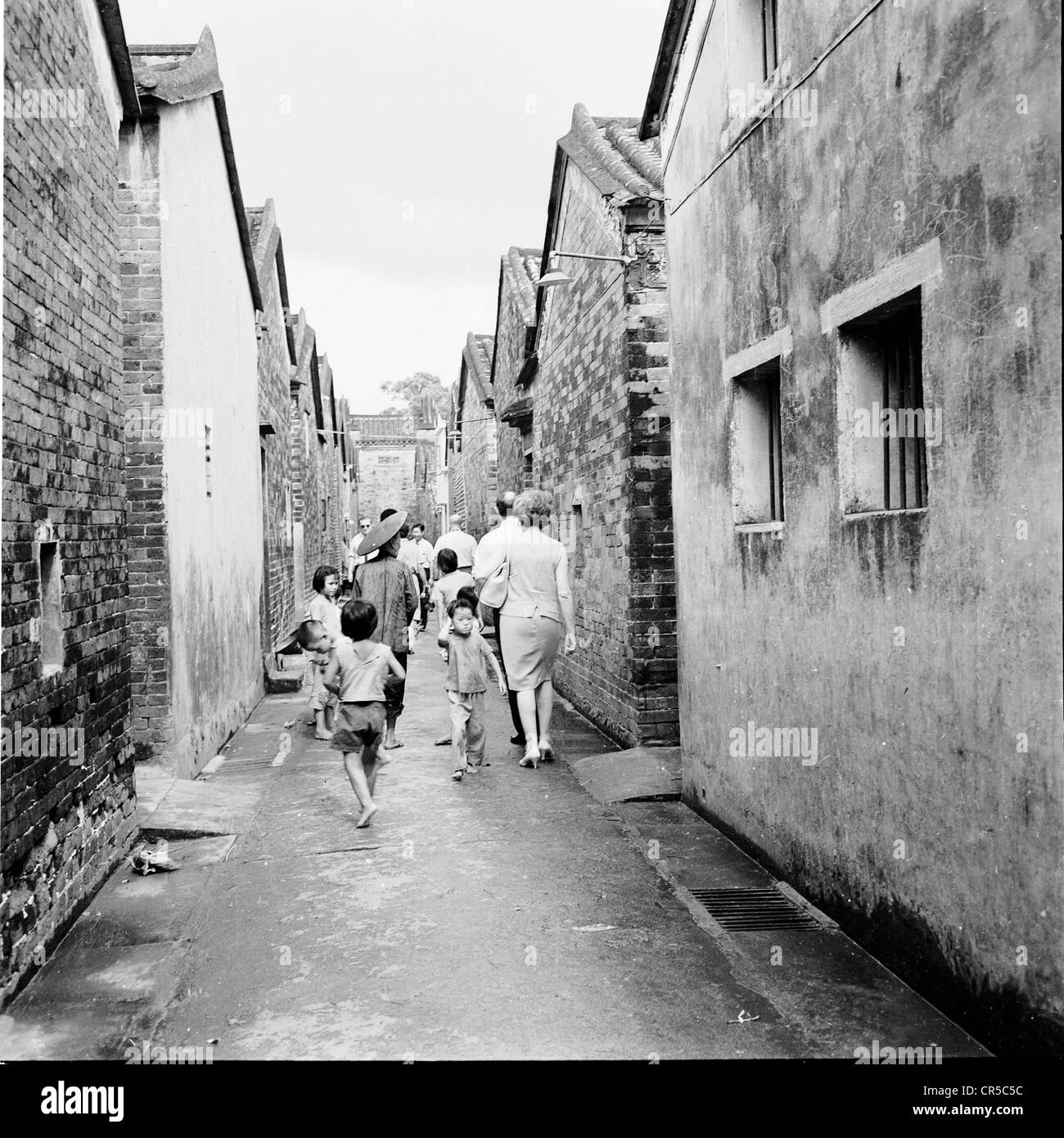 Geschichtsbild aus Hong Kong, 1950er Jahre. Ein westliches paar gehen die hinteren Straßen gefolgt von lokalen chinesischen Kinder. Stockfoto