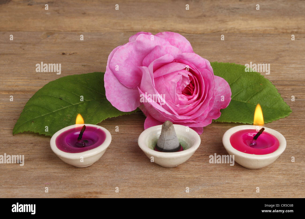 Rosa Rose mit kleinen brennenden Kerzen und Weihrauch auf einem Hintergrund von verwittertem Holz Stockfoto