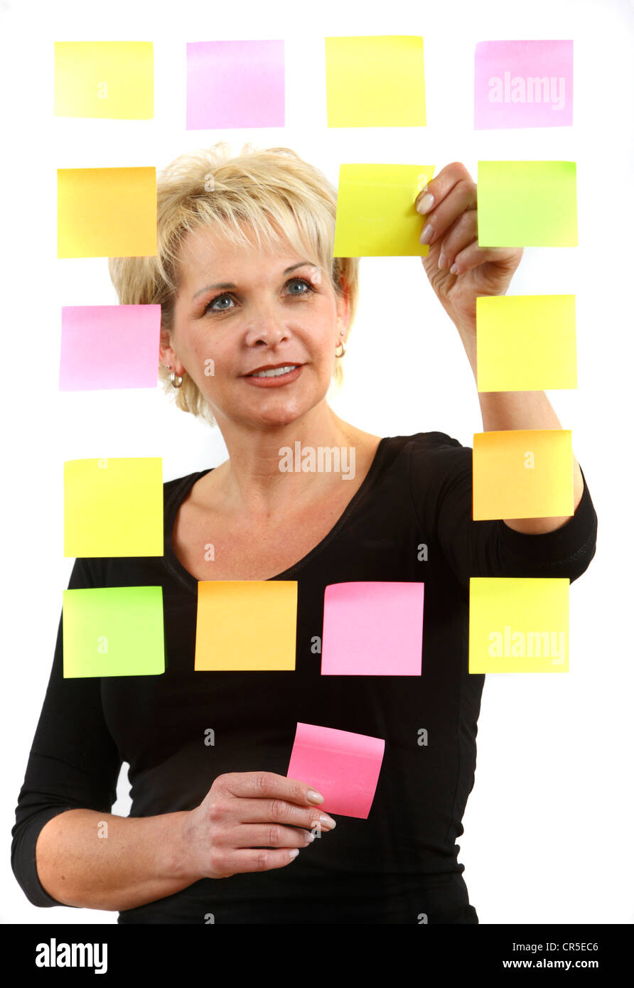 Frau klebt selbstklebenden Post-It, Notizen auf Papier, auf einer Glasscheibe geklebt. Verschiedenen Farben. Stockfoto
