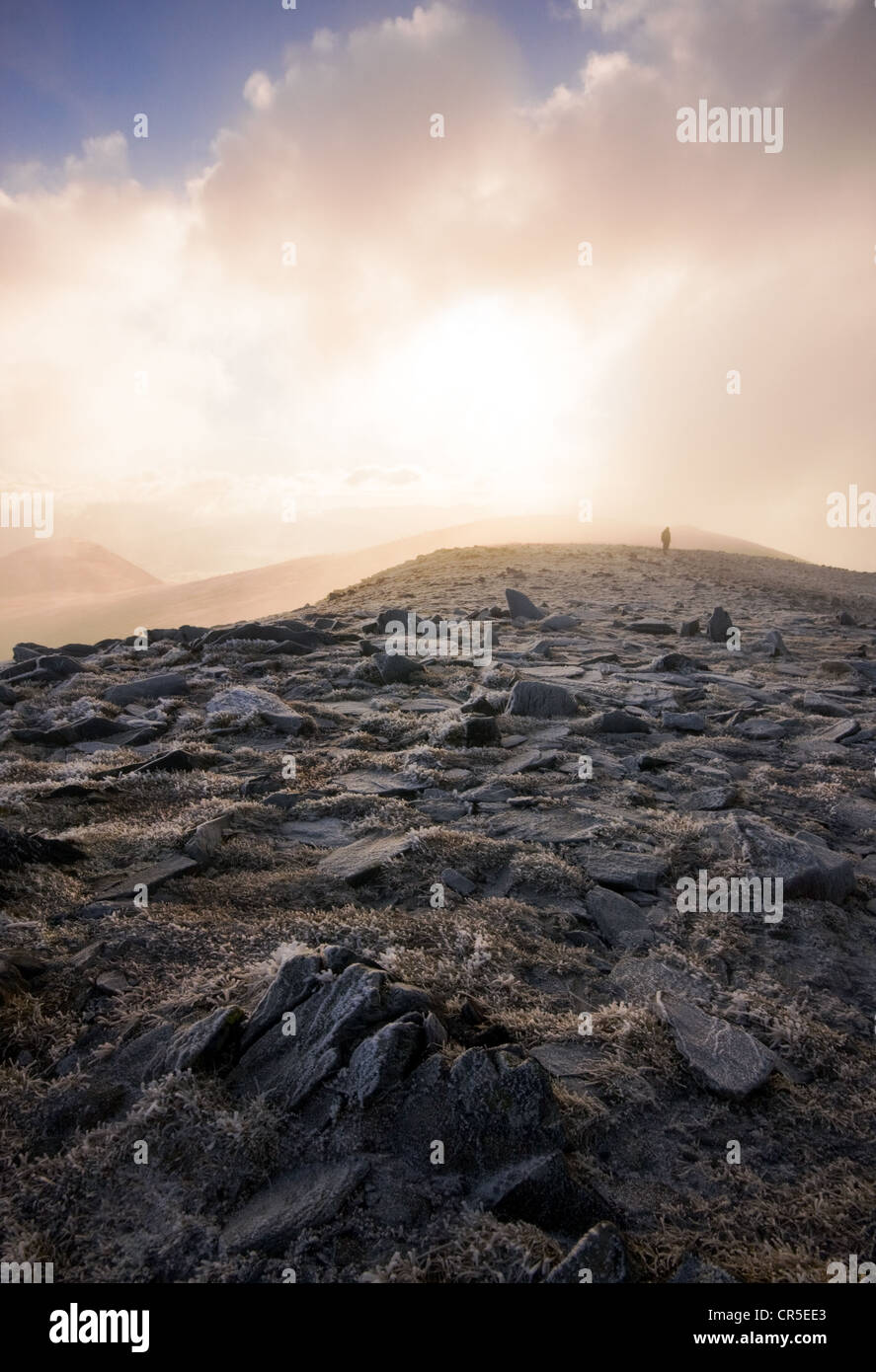 Eine einsame Gestalt auf dem Gipfel des Skiddaw im Lake District wie die Sonne durch die Wolken brechen versucht. Stockfoto