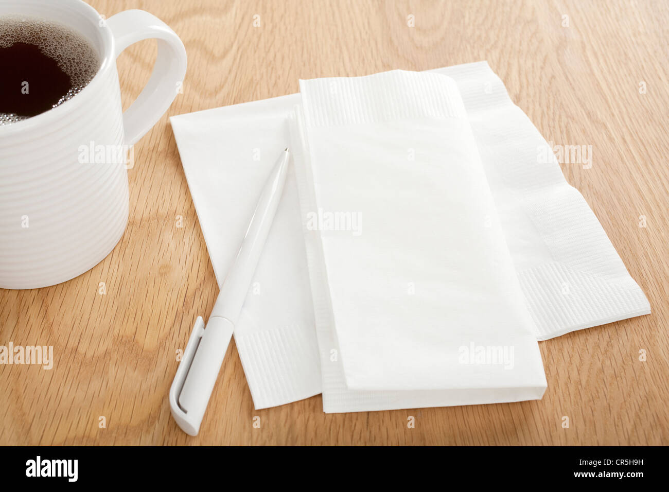 Weißes Papierserviette auf Holztisch mit Stift für Notizen, und Becher Kaffee, Stockfoto