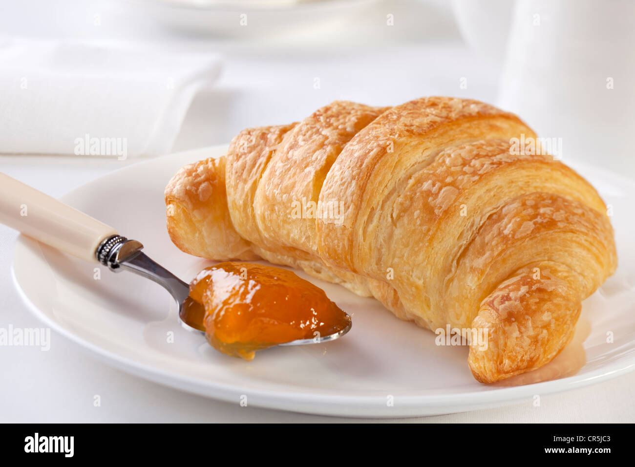 Croissant mit Marillenmarmelade, mit weißen Accessoires. Ein schönes Frühstück! Stockfoto