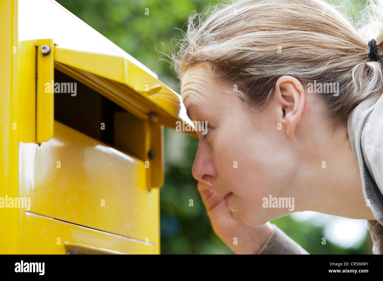 Junge Frau, die neugierig in einen Briefkasten Stockfoto