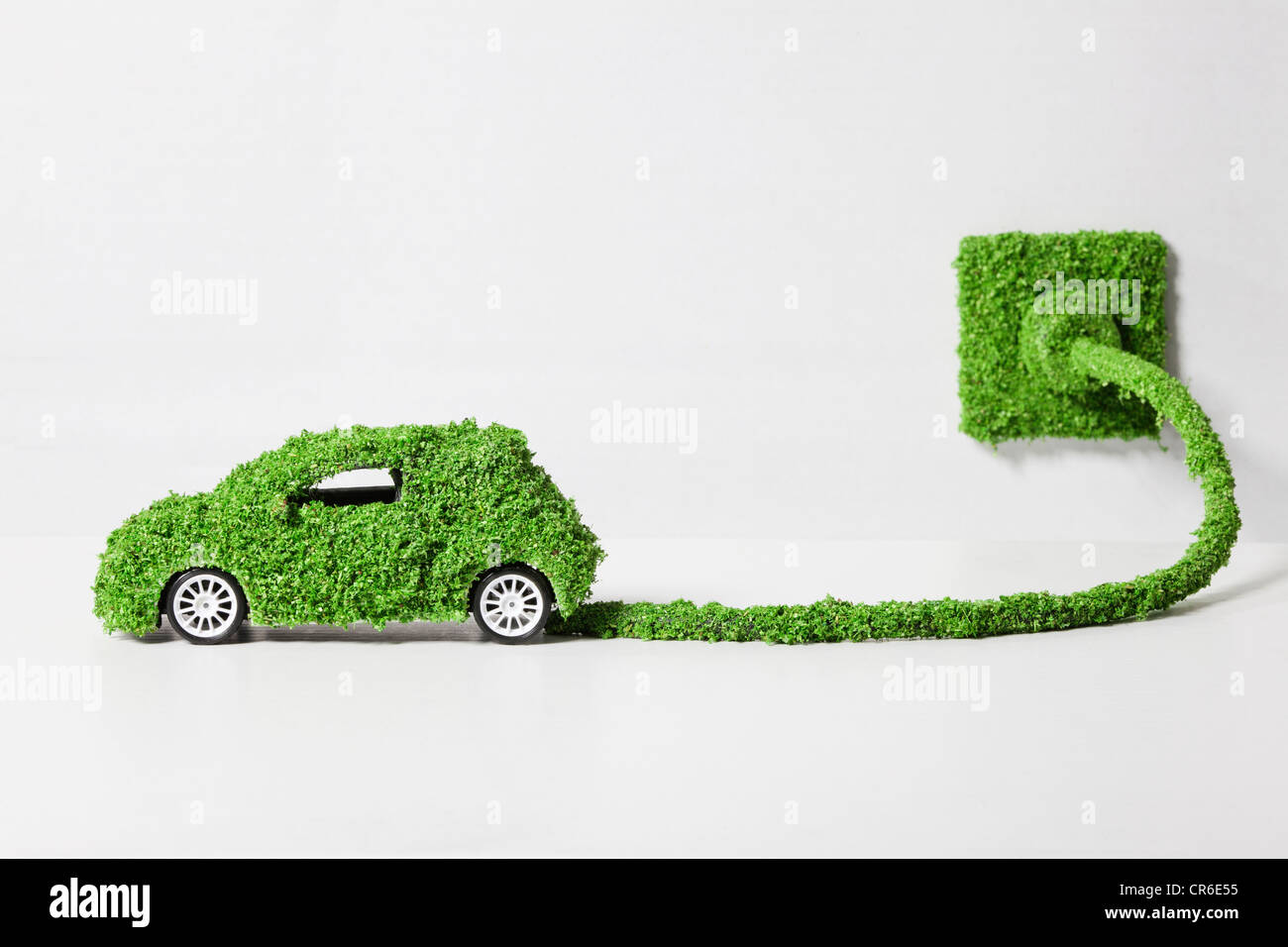 Elektroauto, bedeckt mit Grass verbunden mit Buchse, Nahaufnahme Stockfoto