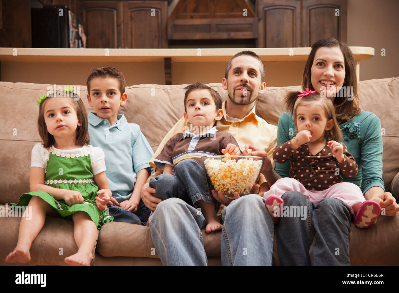 Frontansicht der Familie mit Kindern (18-23 Monate, 4-5, 6-7, 8-9) sitzen auf der Couch vor dem Fernseher und Essen Popcorn Stockfoto
