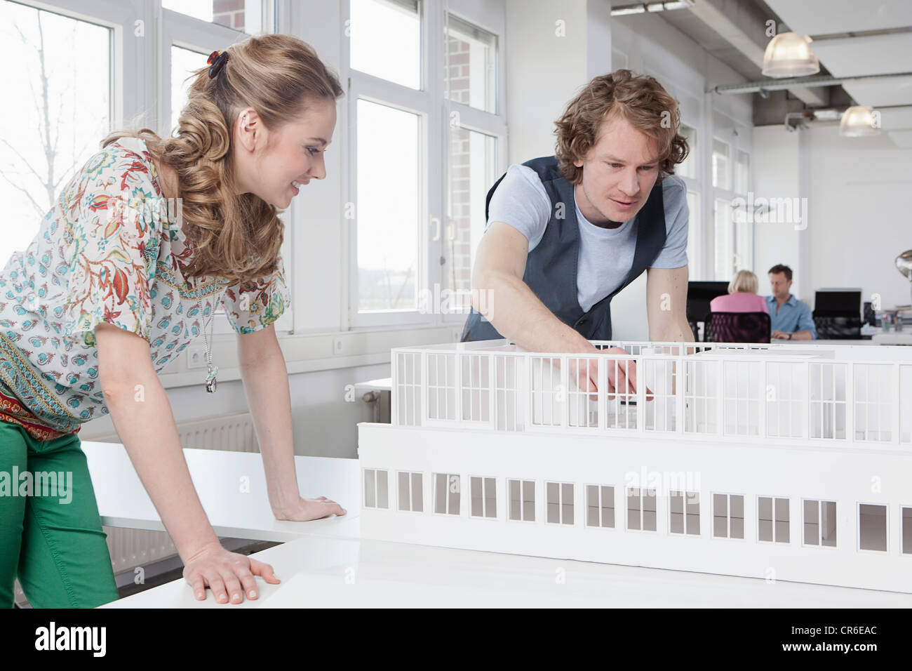 Deutschland, Bayern, München, Architekten betrachten Architekturmodell, im Hintergrund arbeitenden Kolleginnen und Kollegen Stockfoto