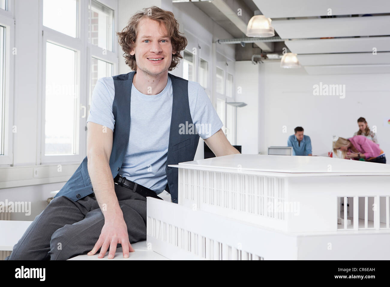 Deutschland, Bayern, München, Architekt mit Architekturmodell, im Hintergrund arbeitenden Kolleginnen und Kollegen Stockfoto